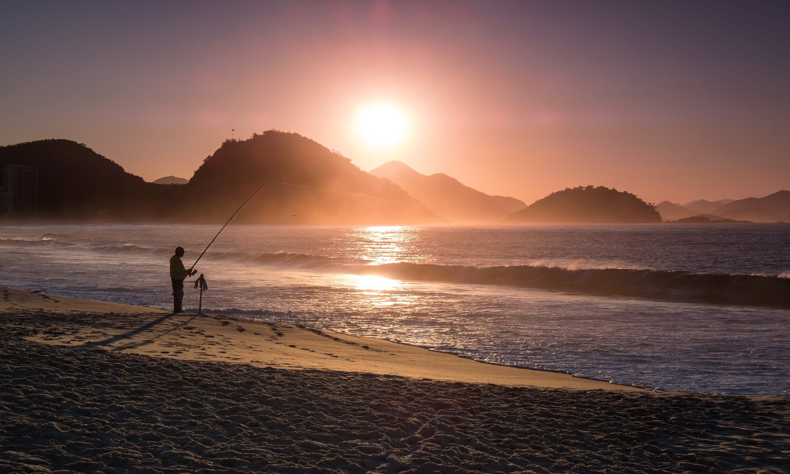 person-fishing-on-the-beach-is-silhouetted-at-sunset